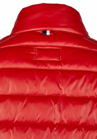 Rote gepolsterte Jacke mit hohem Kragen, horizontalen Nähten und einer kleinen dreifarbigen Akzentschleife im Nacken. Glatte, glänzende Textur.