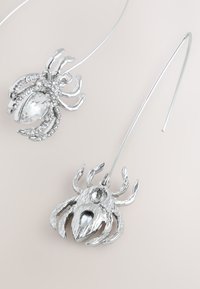 Silver spider-shaped earrings with intricate detailing and clear rhinestone accents. Long, thin hooks for secure wear.