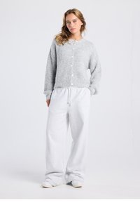 Gray knitted cardigan with a round neckline and front buttons, paired with loose-fitting light gray sweatpants and casual shoes.