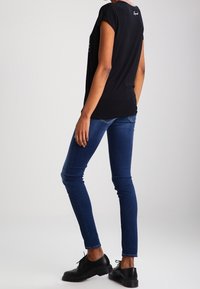 Camiseta negra de manga corta con un ajuste relajado, combinada con jeans azul ajustados y zapatos negros con cordones, mostrando un look simple y casual.