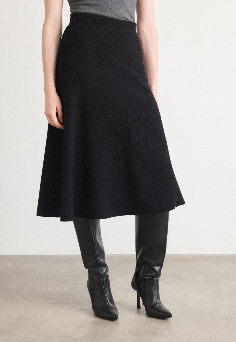 Black flared skirt made of textured fabric, featuring a high waist and curved seams. Paired with knee-high black pointed boots.