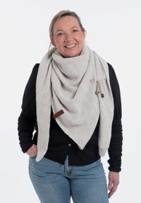 Gehaakte driehoekige sjaal in licht beige, met een textuurpatroon, voorzien van een houten label en een zilveren veiligheidsspeld detail.