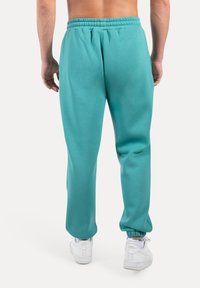 Teal joggingbroek met een elastische tailleband, taps toelopende boorden en zijzakken, gecombineerd met witte sneakers. Zachte katoenen stof textuur.