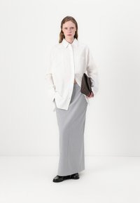 Fehér, oversized gombos ing, szürke maxi szoknya, fekete cipők, sötétbarna clutch táska a kezében. Simogatós textúrák minimalista designnal.