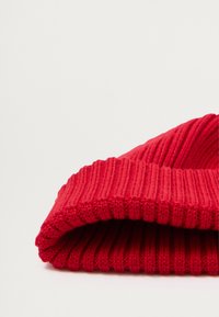 Berretto lavorato a maglia rosso con texture a coste e risvolto. Il materiale sembra morbido ed elastico, progettato per calore e comfort.