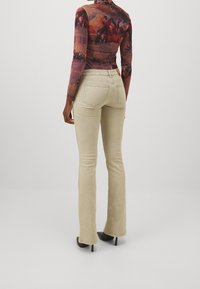 Jeans de campana beige con una textura suave, que cuentan con bolsillos traseros y detalles de costura sutiles. Combinados con una blusa de manga larga ajustada y estampada.