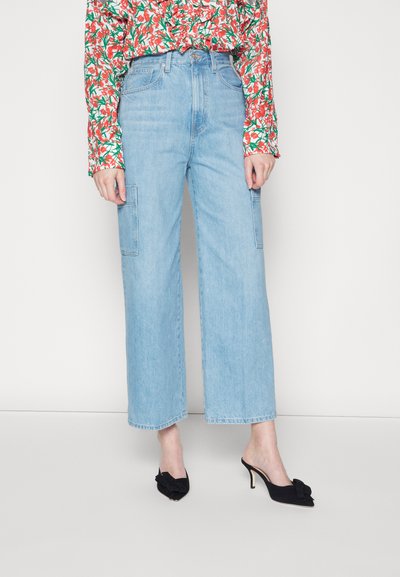 Jeans largos de tom azul claro com cintura alta, apresentando dois bolsos laterais e uma textura de denim suave. Combinados com mules pretos de salto.