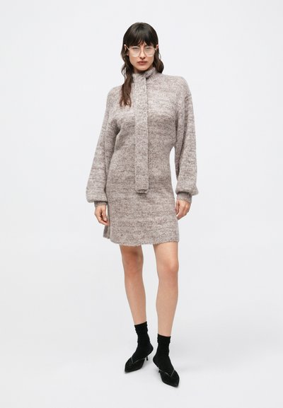 Pletené šaty svetlohnedej farby s golierom, dlhými rukávmi a dĺžkou do polovice stehna. Nosené s čiernymi ponožkami a špicatou obuvou.