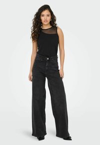 Haut sans manches noir avec des détails transparents au niveau de l'encolure, associé à un jean en denim noir à taille haute et à jambe large.