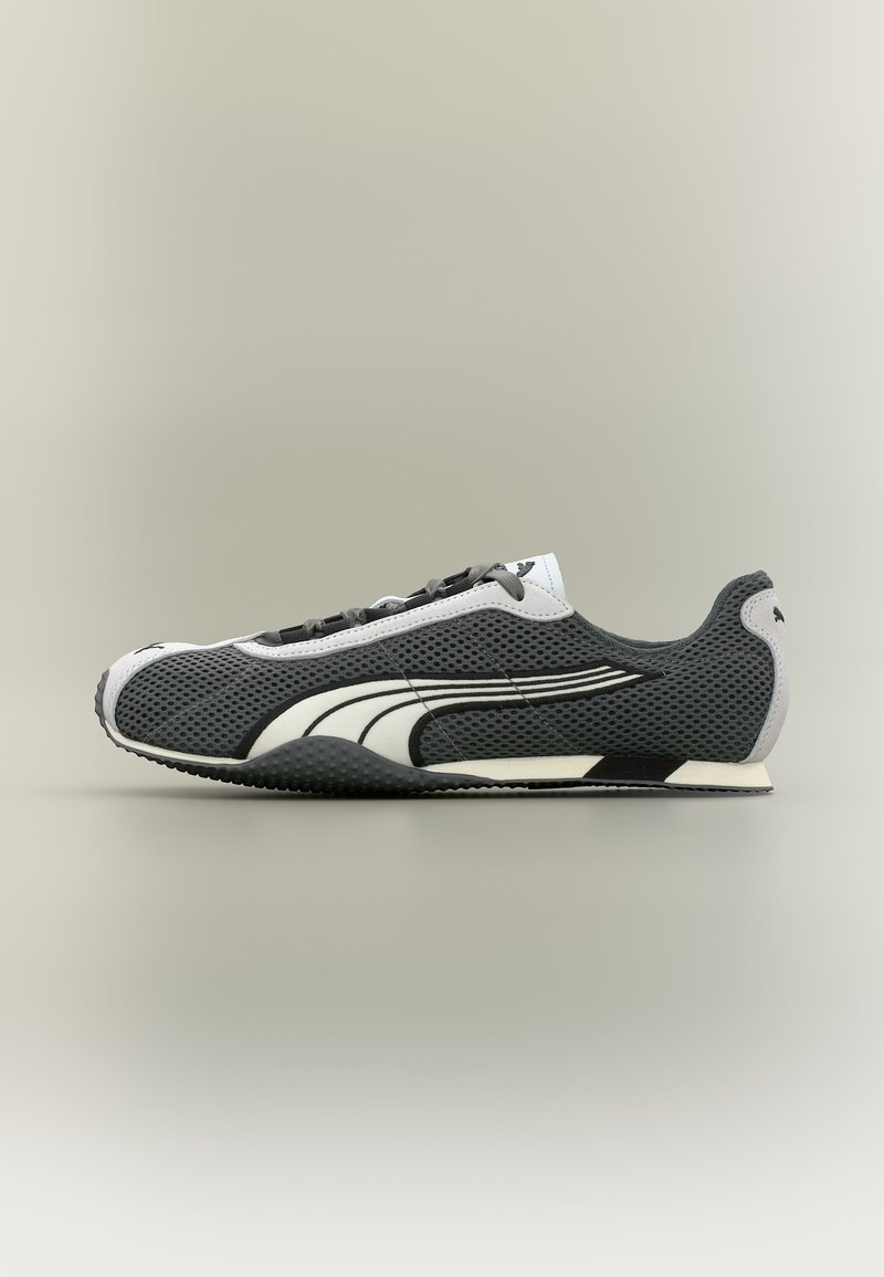 Chaussure de running en mesh noir et blanc avec un design à lacets et un logo blanc incurvé sur le côté, présentée sur un fond neutre.