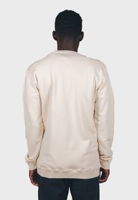 Sudadera color crema con mangas largas y puños acanalados. Presenta un cuello redondo clásico y una textura suave, mostrada desde la espalda.