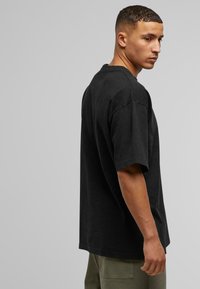Juodas per didelis T-shirt'as su trumpomis rankovėmis ir apvalia iškirpte, pagamintas iš minkštos medvilnės medžiagos, turintis laisvą bortą ir minimalų siūlių skaičių.