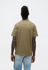 Olíva zöld színű pamut póló, környakú, rövid ujjú, laza fazonú. Enyhe textúrájú, egyszerű, minta nélküli kialakítás.