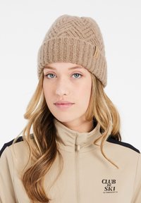 Berretto lavorato a maglia beige con motivo a trecce, dotato di un piccolo etichetta in pelle. Texture liscia, vestibilità aderente e design con risvolto.