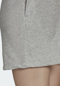 Detailní záběr osoby v světle šedé pletené sukni, ukazující strukturu látky a detail bočního švu.