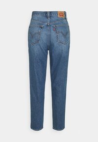 Jean en denim bleu avec une coupe droite, taille haute et poches arrière ornées d'un motif de couture signature et d'une étiquette de marque.