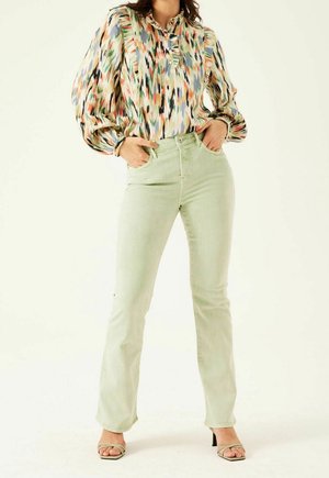 Blouse multicolore à manches longues avec un plastron boutonné, associée à un jean ajusté vert clair et des sandales à talons. Texture lisse, coupe décontractée.