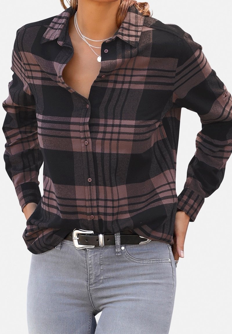 Femme portant une chemise à carreaux noire et marron boutonnée, rentrée dans un jean gris clair avec une ceinture noire et une boucle argentée.