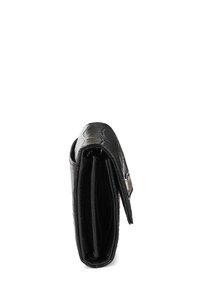 Melnas, spīdīgas krokodila tekstūras maks, kas stāv vertikāli, parādot savu sānu profilu ar redzamu atloku un iekšējām kabatām.