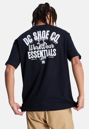 Zwart katoenen T-shirt met witte grafische tekst op de achterkant, met de tekst "DC SHOE CO. WorkWear ESSENTIALS," en een sterontwerp.