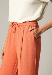 Oranje gekreukt stoffen broek met een elastische tailleband, trekkoorddetails en zijzakken. Glad oppervlak, losse pasvorm.