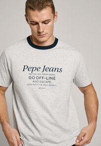Pilkas medvilnės marškinėliai su tamsiai mėlynu apykakle. Su "Pepe Jeans" prekės ženklu ir tekstu tamsiai mėlyna spalva. Atsitiktinė forma, trumpomis rankovėmis.