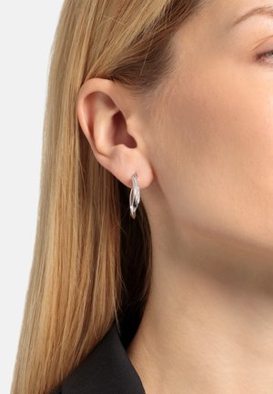 Orecchino a cerchio in argento con un design torcido, caratterizzato da un accentuato texture. L'orecchino pende dal lobo, riflettendo la luce.