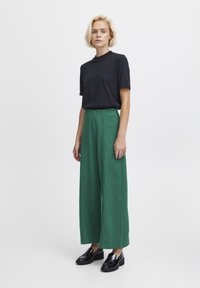 T-shirt nera a maniche corte abbinata a pantaloni larghi a quadri verdi e mocassini neri lucidi. Design semplice e moderno con una vestibilità rilassata.