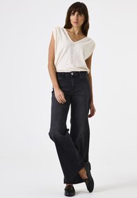 Top blanco de manga corta y escote en V, combinado con jeans de pierna ancha de denim oscuro y cintura alta. Mocasines negros con detalles en dorado.