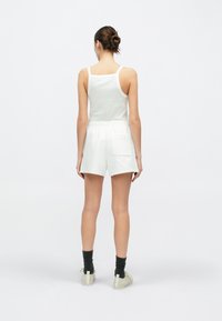 Débardeur blanc et short assorti en tissu doux. Le short comprend une ceinture élastique et une poche arrière. Porte avec des chaussettes foncées et des chaussures claires.