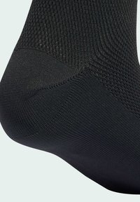 Primo piano di un tessuto nero texturizzato sulla zona del tallone e della caviglia di una calza, con diversi motivi di lavorazione per supporto e traspirabilità.