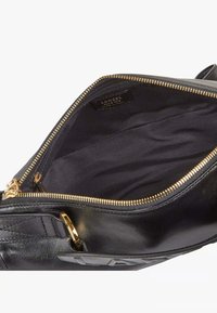 Εσωτερικό μαύρης δερμάτινης τσάντας με χρυσό φερμουάρ. Διαθέτει υφή επένδυσης και μια ετικέτα ορατή μέσα. Ανοιχτός σχεδιασμός που δείχνει ευρύχωρο χώρ ο.