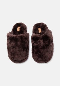 Ζευγάρι σκουρόχρωμων καφέ παντόφλες με αφράτη υφή, χωρίς πίσω μέρος, με απαλό υλικό και ανοιχτόχρωμες εσωτερικές ετικέτες, τοποθετημένες σε λευκή επιφάνεια.