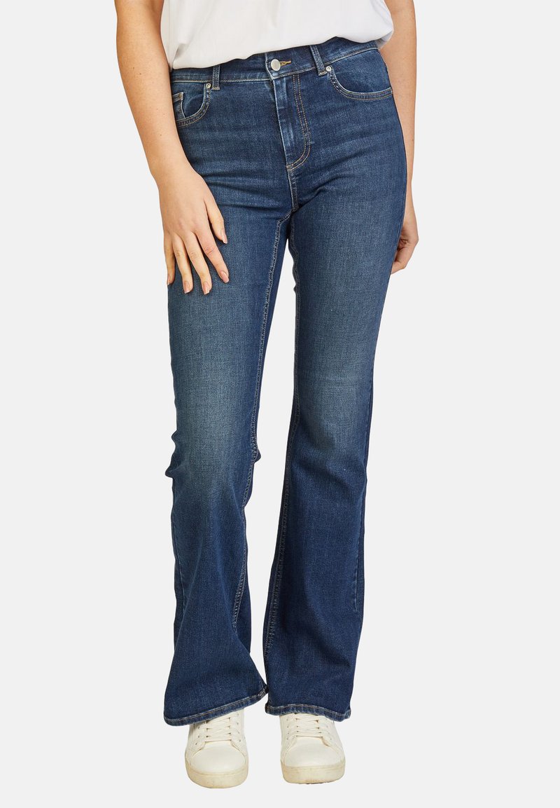 Donkerblauwe denim flared jeans met een middelhoge taille, zichtbare stiksels en een lichte stretch. Draagt met witte sneakers.