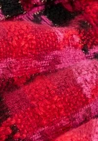 Tessuto strutturato in tonalità di rosso, rosa e nero, caratterizzato da una superficie pelosa con schemi e profondità variabili, creando interesse visivo.