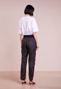 Vitt oversized t-shirt tillsammans med svarta byxor med prickar, som har en dragsko i midjan och röda sidostrikar. Lätta klackar fulländar looken.