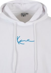 Bílá mikina s kapucí s modře vyšitým textem. Materiál je měkký, s šňůrkami a viditelnou etiketou uvnitř. Jednoduchý design, bez vzorů.