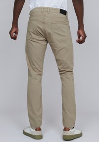 Pantalons beiges à jambes droites au design classique, dotés de poches arrière et d'une ceinture texturée, associés à des baskets blanches.