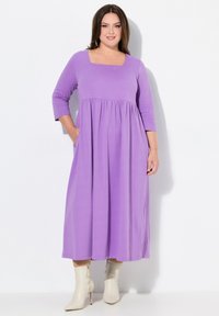 Lila, polvipituinen mekko, jossa on kolme nelj�änneshihaa, neliönmuotoinen kaula-aukko, kerätty vyötärö ja sivutaskut, yhdistettynä vaalean kermaisiin nilkkasaappaisiin.