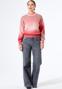 Gebreide trui in een gradient roze, met een textuurpatroon, ribbelmanchetten en een hoge hals. Gecombineerd met grijze wijde jeans.
