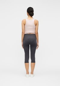 Débardeur ajusté rose clair et leggings capri gris foncé. Tissu en mélange de coton lisse. Design simple avec une longueur raccourcie et une ceinture élastique.