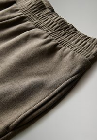 Primo piano della cintura elastica marrone e della tasca laterale su pantaloni in tessuto morbido, che mostrano texture e dettagli di cucitura.