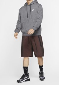 Grå hoodie med dragsnören och framficka, kombinerad med röd och svart rutiga shorts. Svarta sneakers och strumpor med logotyp-accenter.