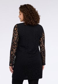 Schwarzes Spitzenkleid mit langen transparenten Spitzenärmeln mit floralem Muster, einem taillierten Oberteil und einem leicht ausgestellten Saum.