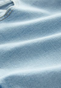 Primă de material albastru deschis, în prim-plan, având o textură netedă și un model subtil de țesătură denim. Fără hardware sau accente vizibile.