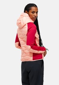 Chaqueta tipo puffer con un respaldo acolchado rosa y mangas color burdeos, que cuenta con capucha, tejido texturizado y un diseño ajustado, llevada sobre pantalones negros.