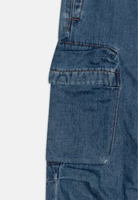 Modre denim cargo hlače z velikim stranskim žepom, s stikanim detajli in rahlo uničenim izgledom. Abrasija na robovih tkanine.