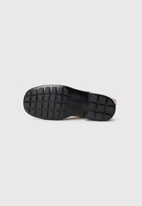 Suola di una scarpa marrone chiaro con suola in gomma nera che presenta un motivo a battistrada rettangolare su uno sfondo bianco.