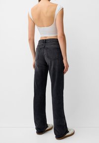 Top corto blanco con la espalda baja, combinado con pantalones de mezclilla negros de pierna ancha que tienen dos bolsillos traseros. Los zapatos tienen una parte superior blanca y suela de goma.