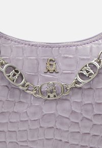 Gros plan sur du cuir lilas embossé croco avec une chaîne argentée présentant des maillons entrelacés du logo SA et une petite plaque logo SA.